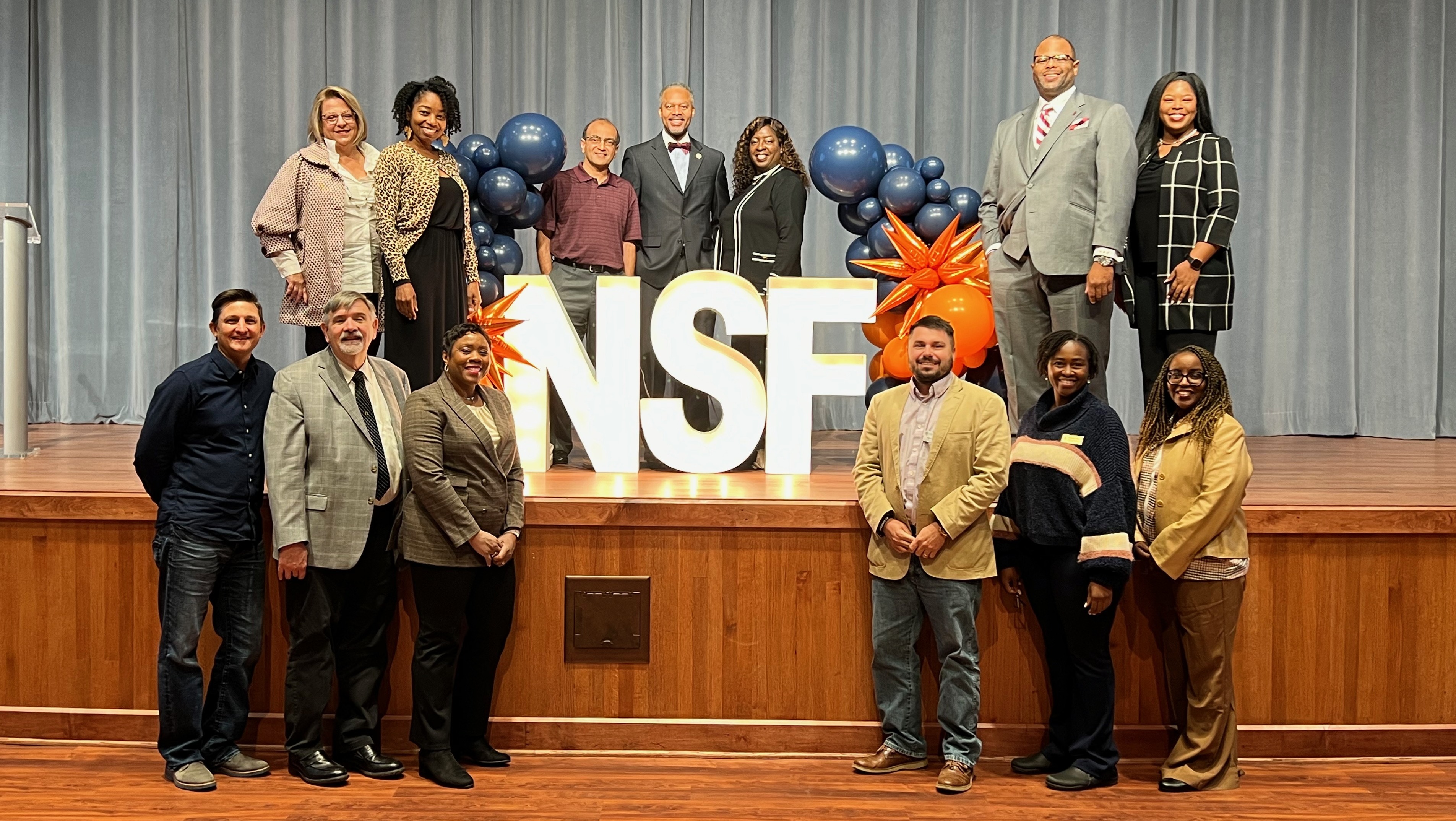 NSF representatives and Auburn researchers gathered around NSF signage on a stage.